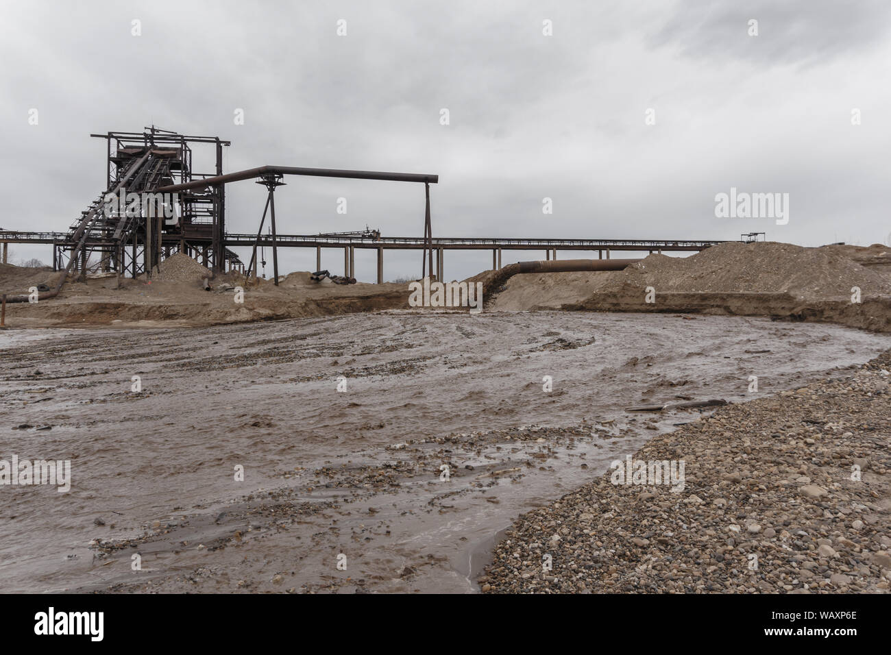 rusty pipe on the river bank, from which sewage flows, dirty sand slurry, and stationary rusty gravitational sand and gravel separator on the foregrou Stock Photo