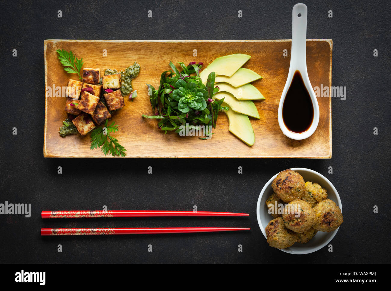 plate decorated with tofu, vegetables and avocado on black stone with falafel and Chinese chopsticks Stock Photo