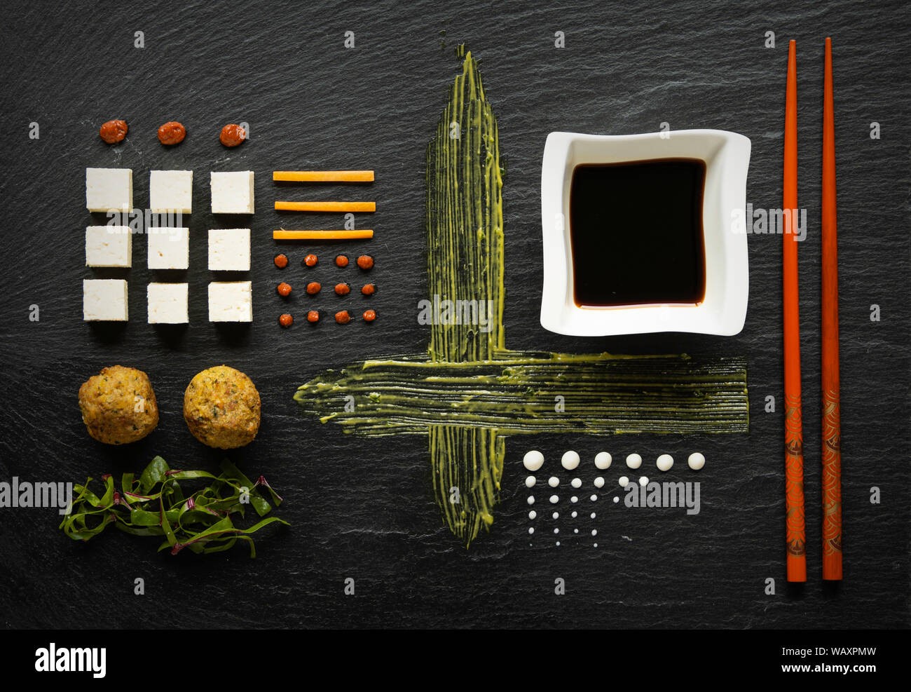ofu cubes on black stone with sauce, vegetables and falafel, in a modern and geometrical arranged Stock Photo