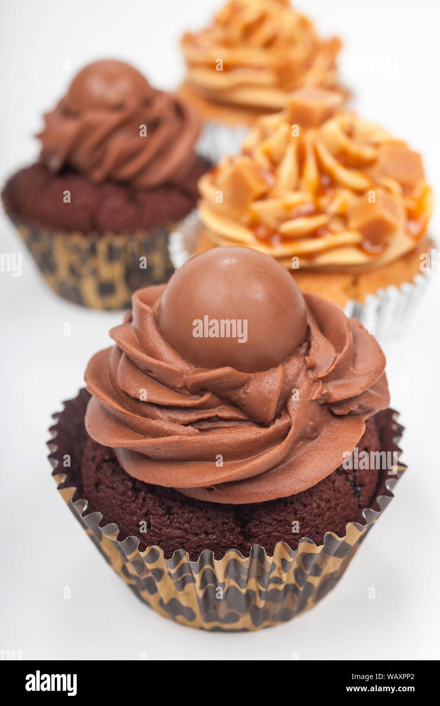Four cup cakes with frosting or icing, two chocolate and two caramel, photographed on a white background Stock Photo