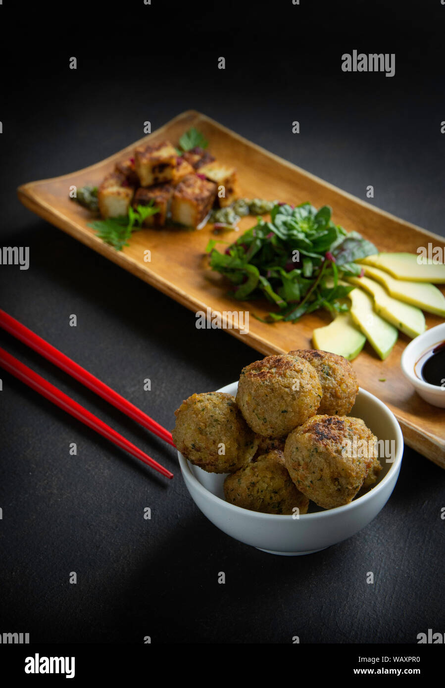 vertical photo of tofu with falafel, vegetables on dish of larch on black background with chopsticks Stock Photo