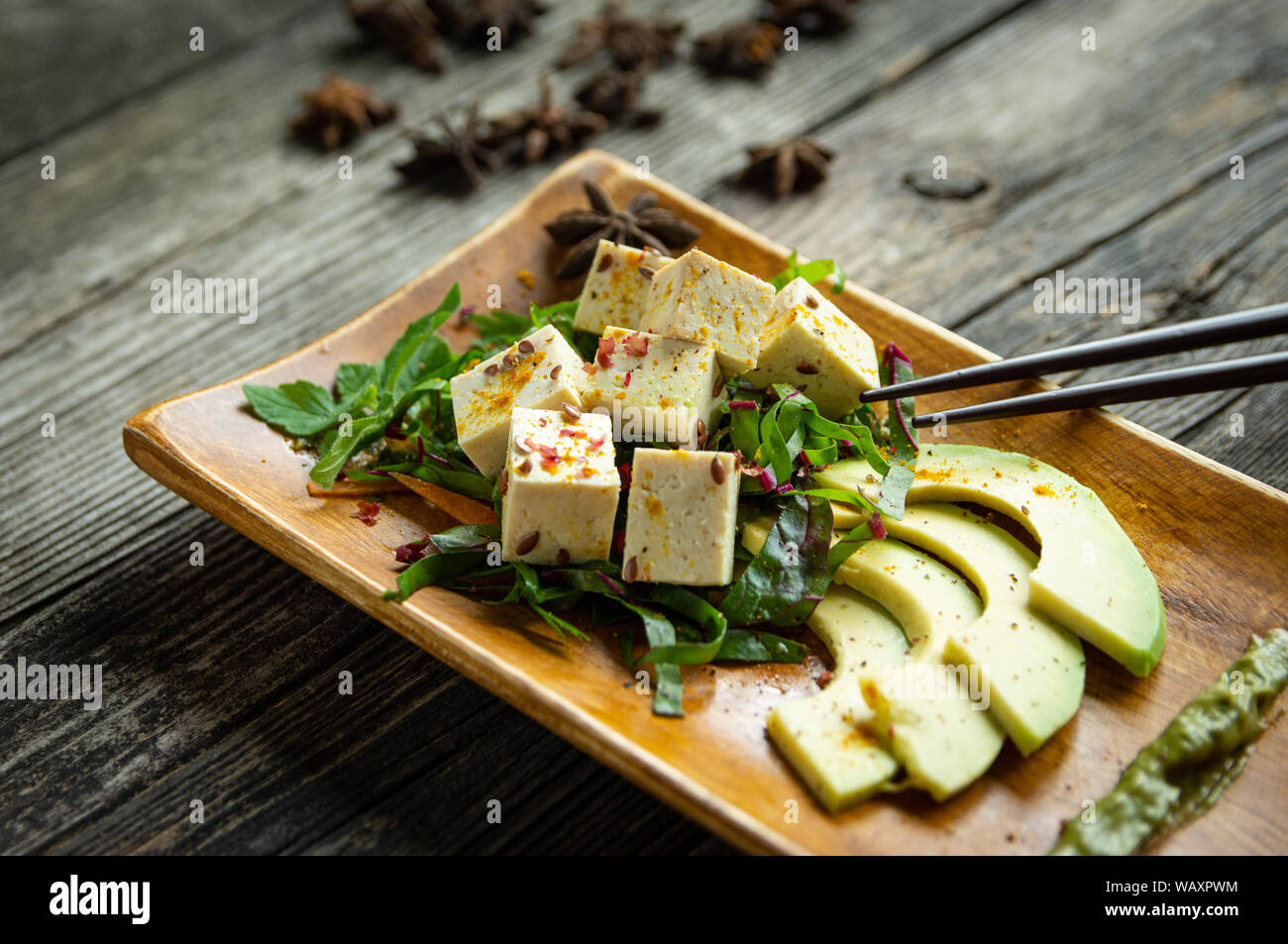 plate of tofu with fresh vegetables and avocado on plate and wooden table Stock Photo