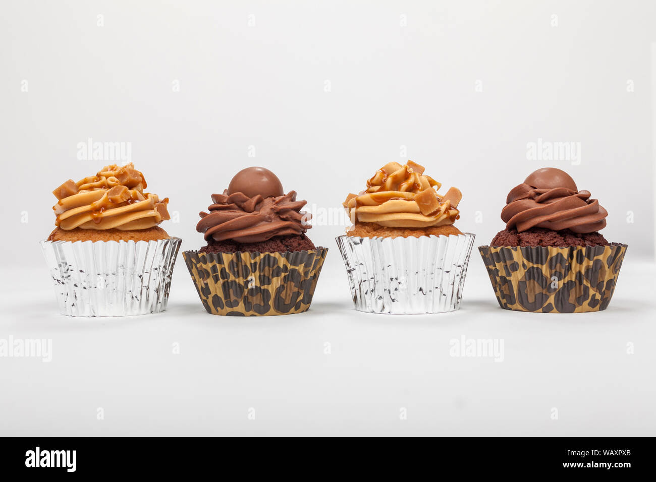 Four cup cakes with icing or frosting, two chocolate and two caramel, photographed on a white background Stock Photo