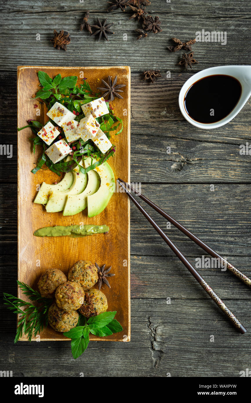 tofu and falafel with fresh vegetables, avocado and spices on a plate and wooden table, view from above, oriental style Stock Photo