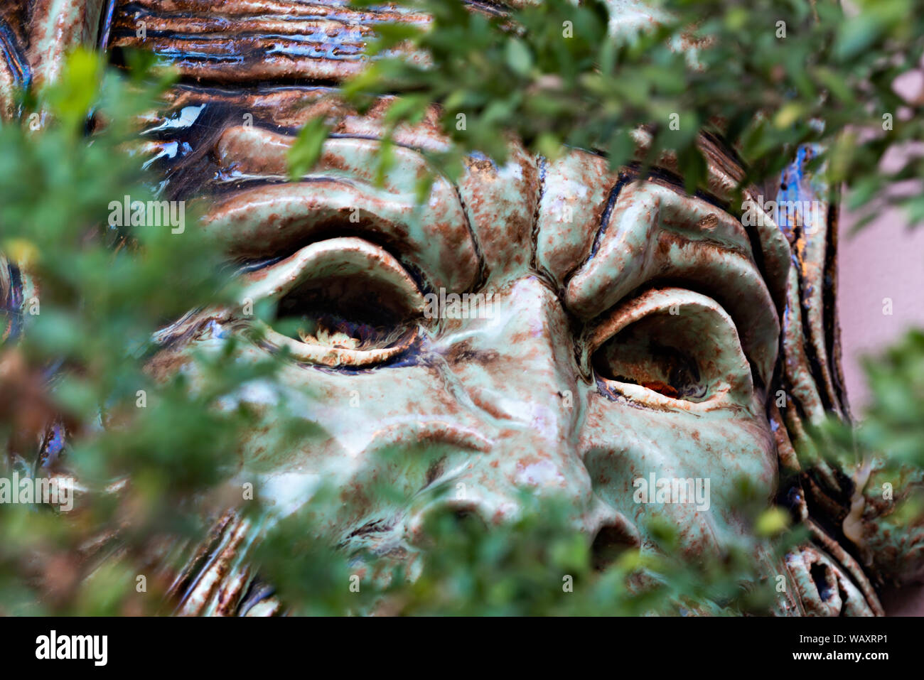 Ceramic face looking through the bushes in the garden Stock Photo