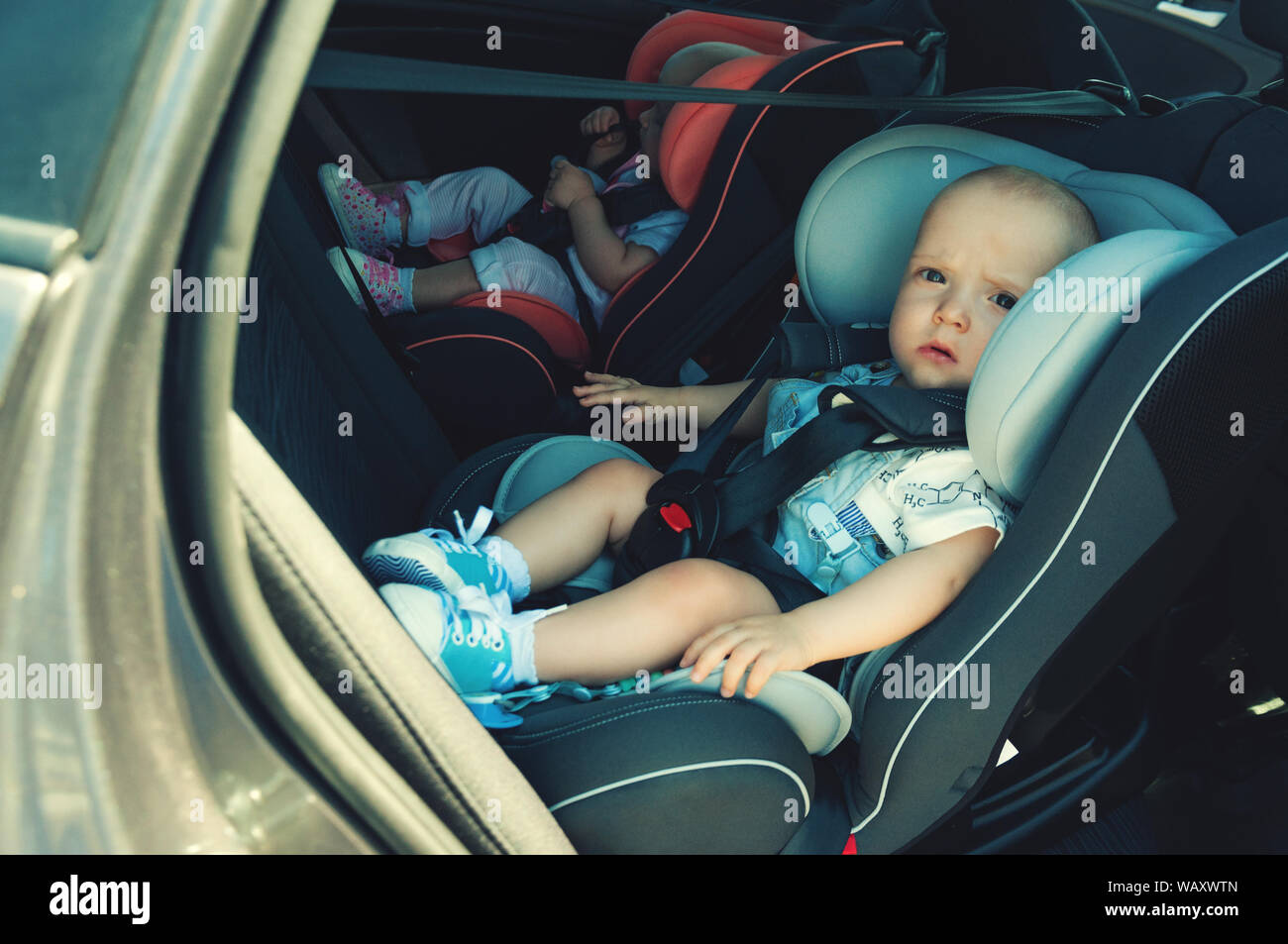 Twins boy and girl in child seats in the car. Safety transportation for babies. Children up to a
