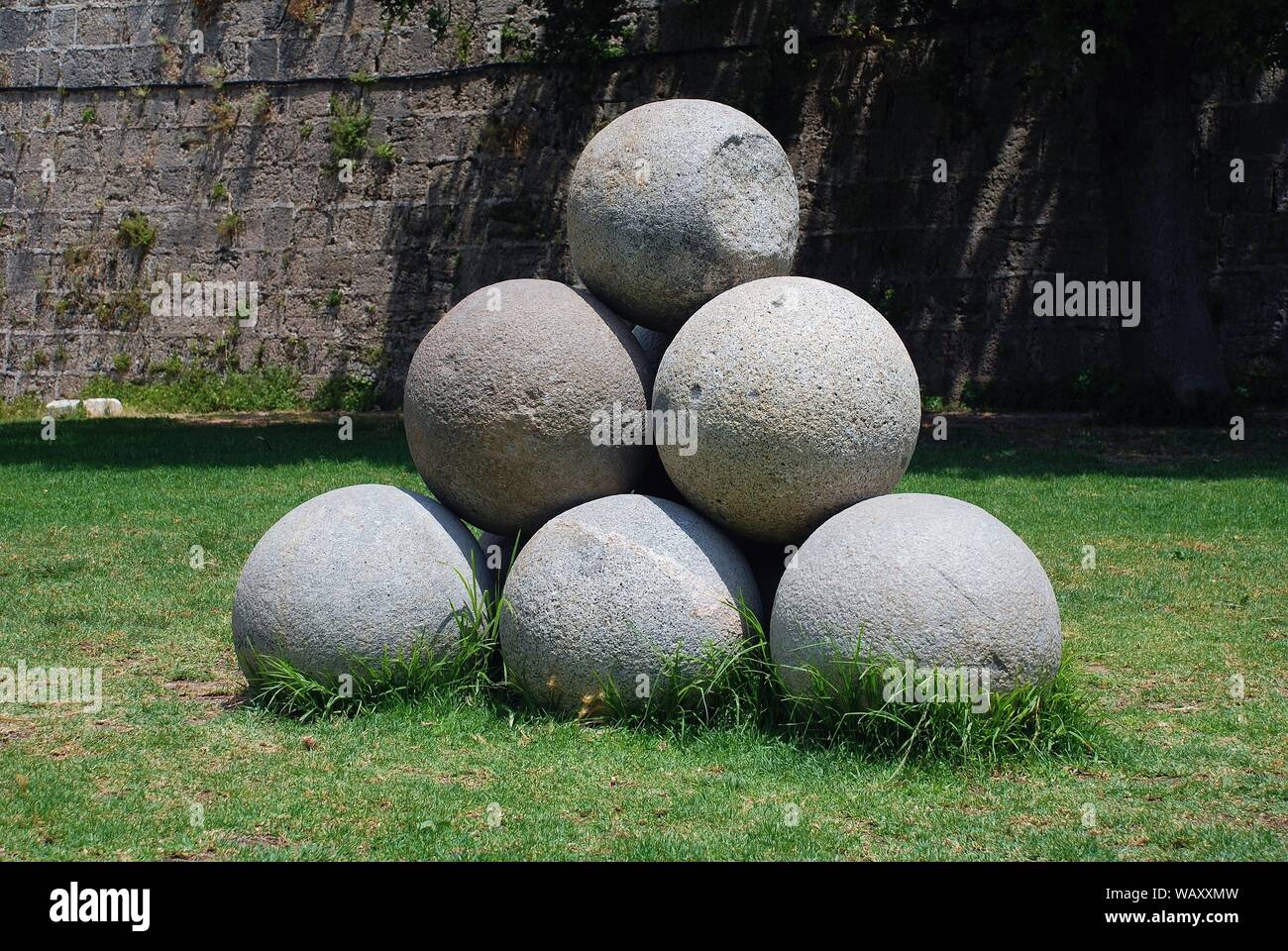 A pile of old stone cannonballs in the drained moat surrounding the medieval wall of Rhodes Old Town on the Greek island of Rhodes. Stock Photo