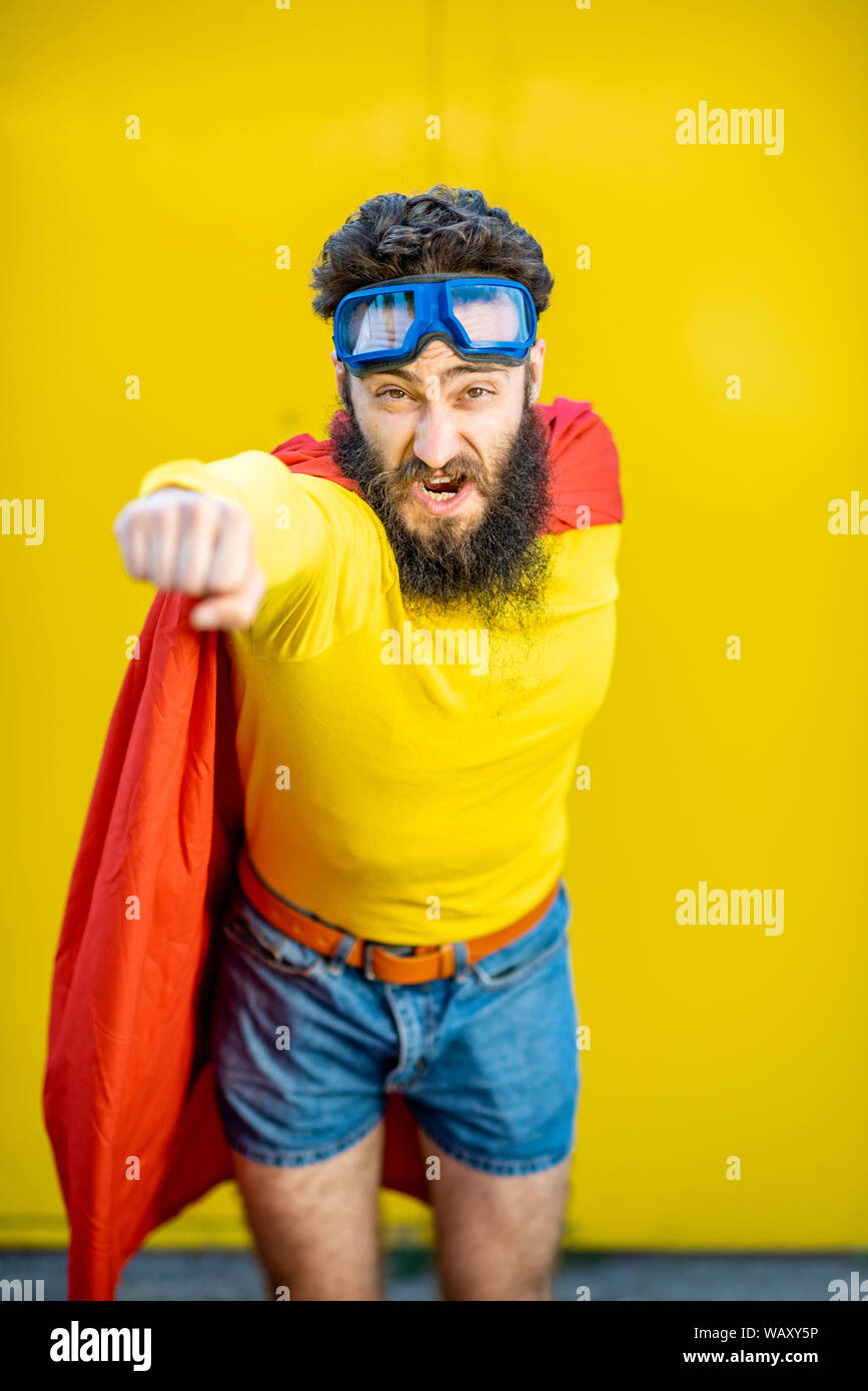Portrait of a man like a superhero in colorful clothes and pilot's glasses on the yellow background Stock Photo