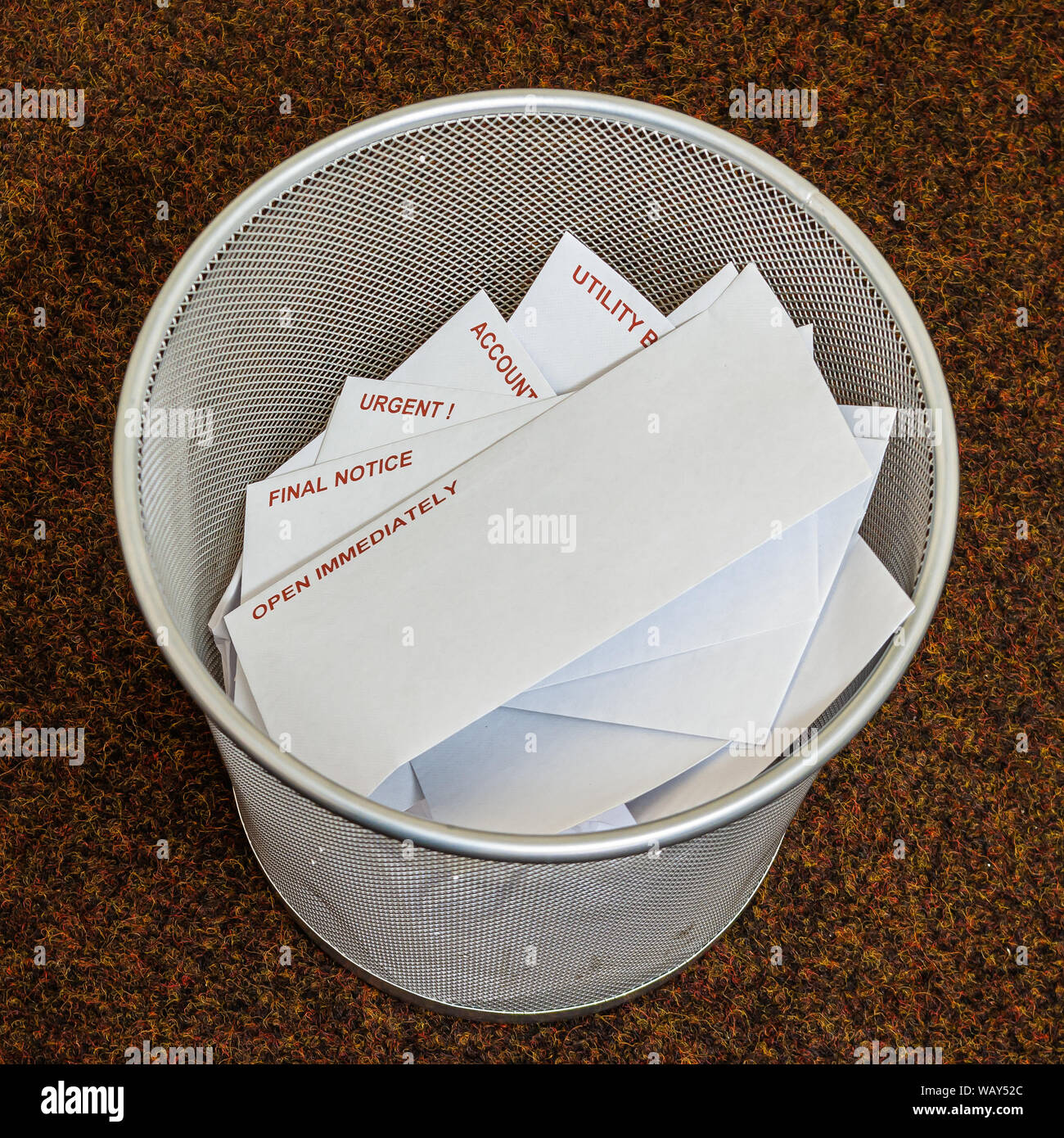 Multiple bills in white envelopes placed in a metal mesh bin on a brown carpet Stock Photo