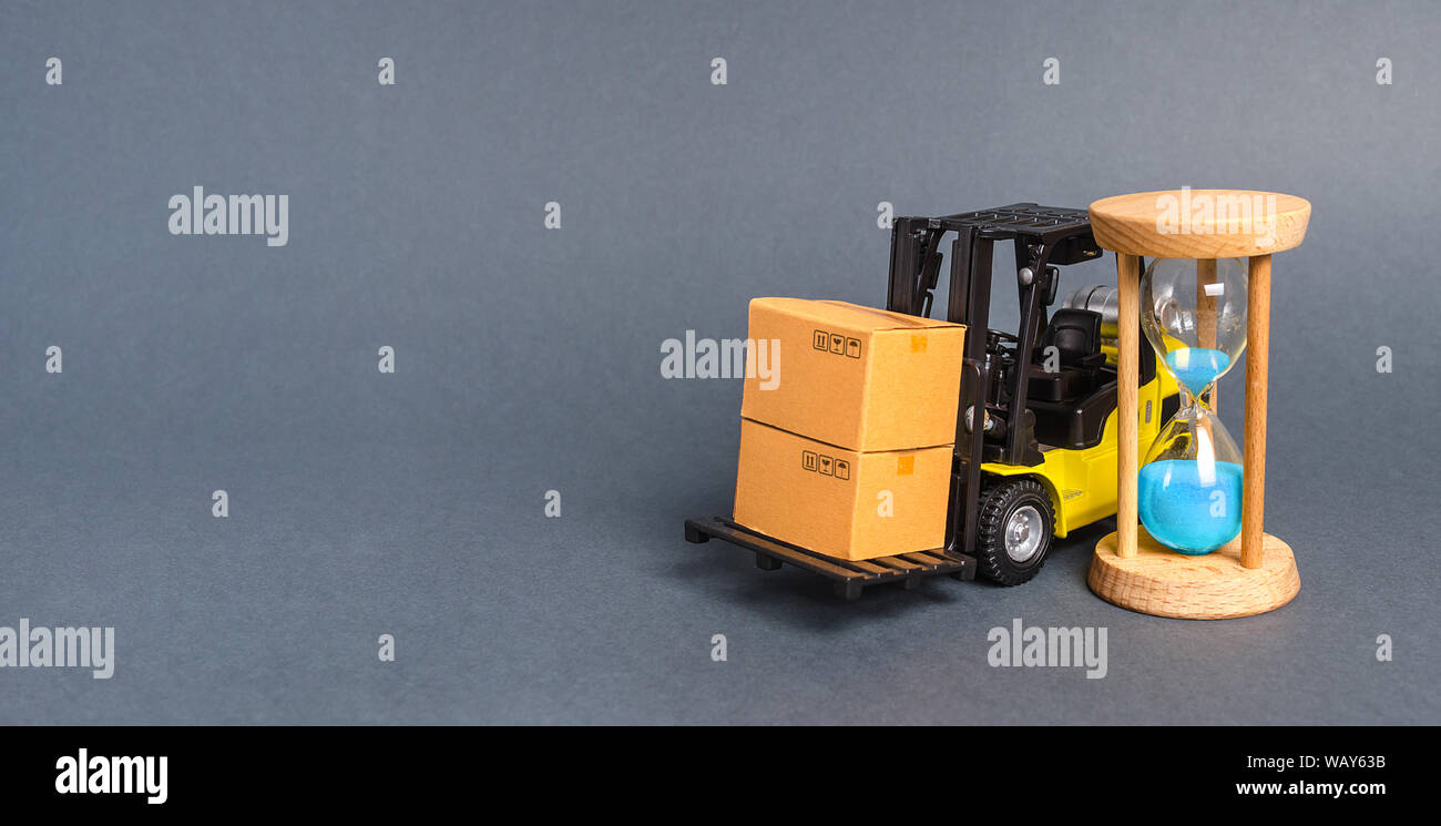 A forklift truck carries cardboard boxes and an sand hourglass. Express delivery in short time concept. Temporary storage. Optimization delivery logis Stock Photo