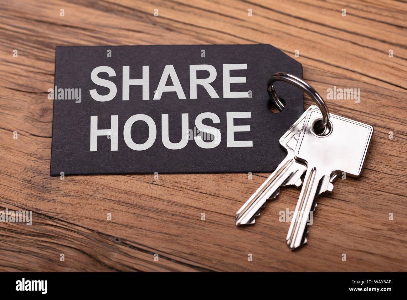 Share House Keys With Black Keychain On Wooden Desk Stock Photo