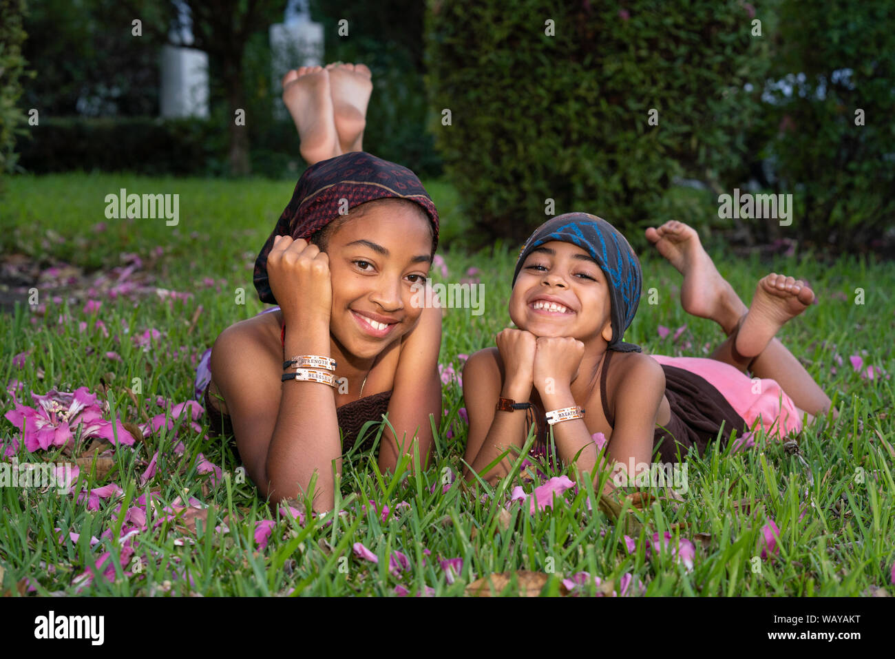 Portrait of two mixed race sisters resting on the grass and smiling at the camera Stock Photo