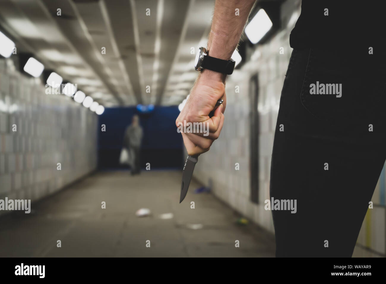 Crime robbery concept. A robber or a killer person with a sharp knife about to commit a homicide in a tunnel. Stock Photo