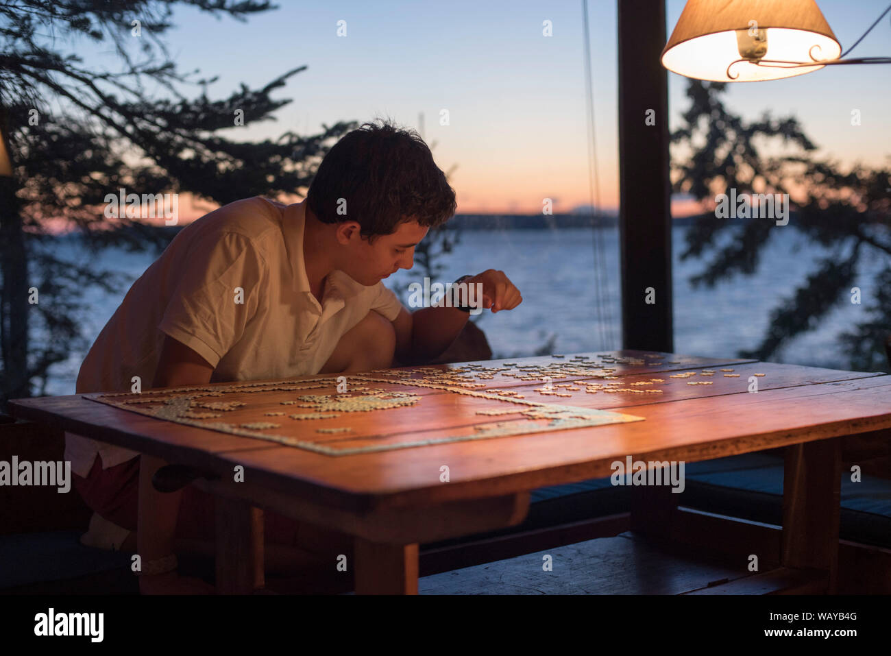 Teenage Boy Doing Jigsaw Puzzle at Lake House at Sunset Stock Photo