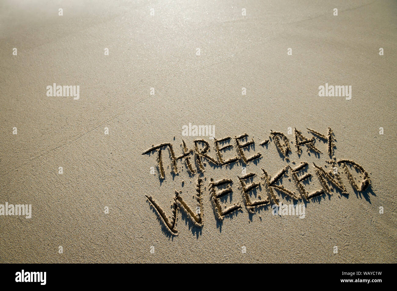 Three-Day Weekend message handwritten on the shore of a beach with smooth sand copy space Stock Photo