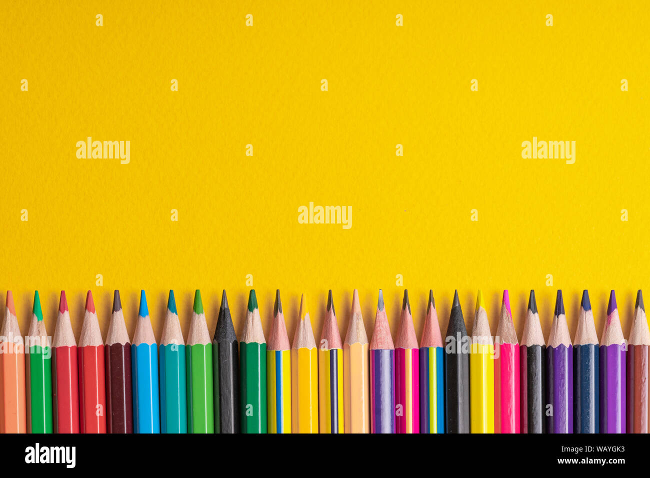 Many sharpened colored pencils laid out on a yellow background. Copyspace Stock Photo