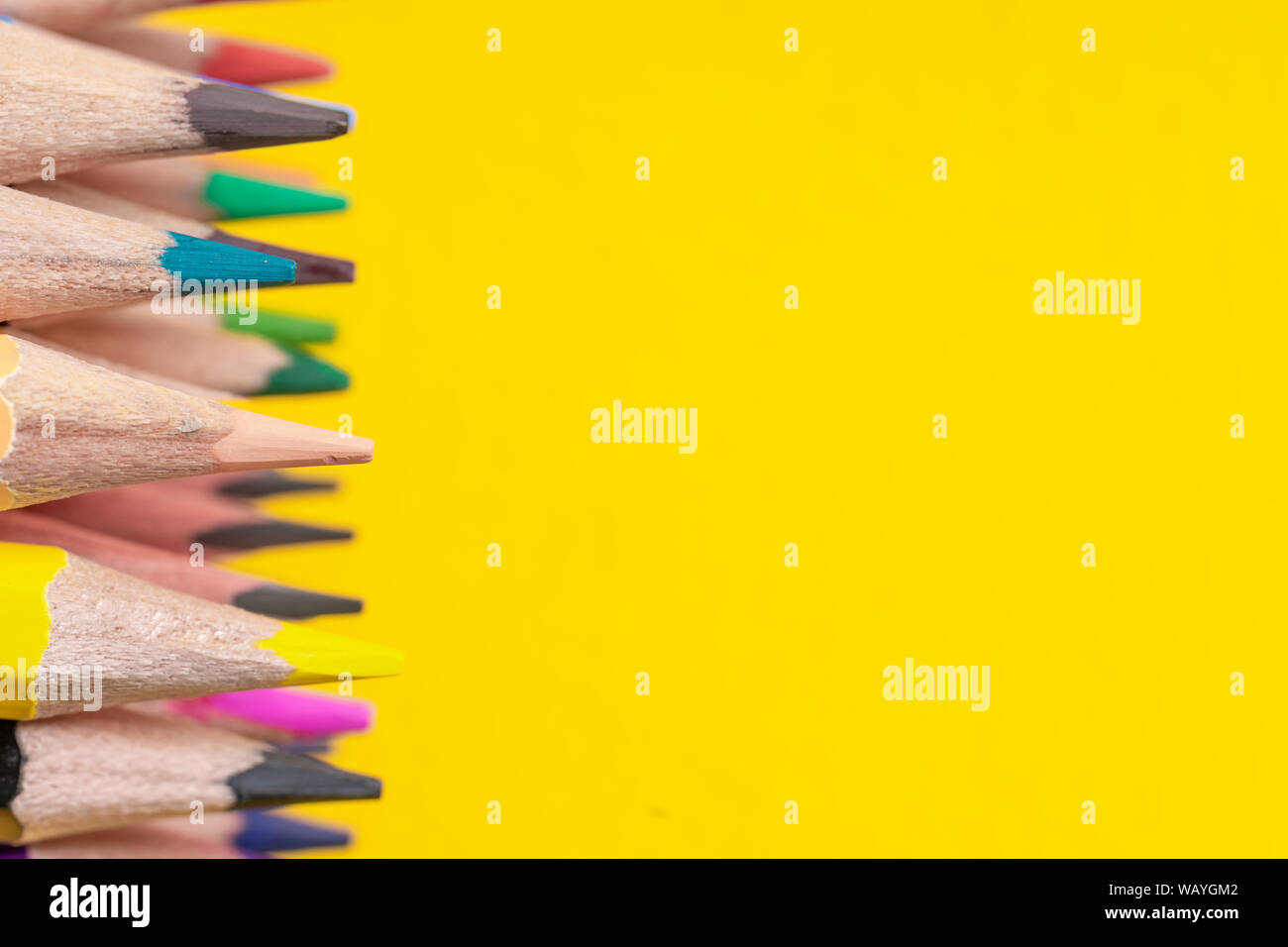 Many sharpened colored pencils laid out on a yellow background. Copyspace Stock Photo