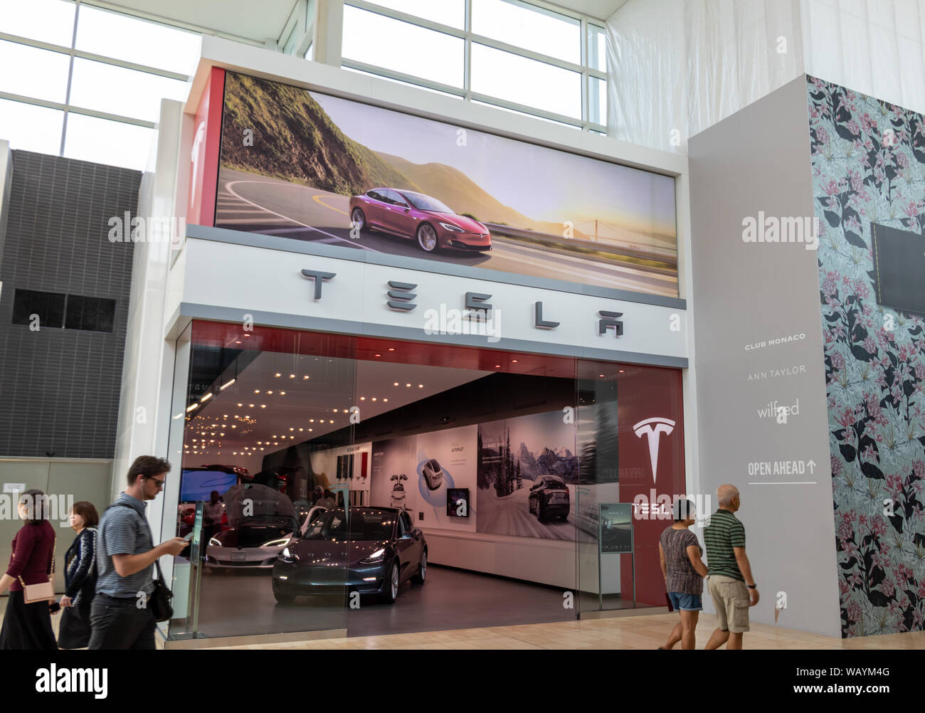 People walk by Tesla Store in Toronto's Yorkdale Shopping Centre with grey Tesla Model 3 inside the store. Stock Photo
