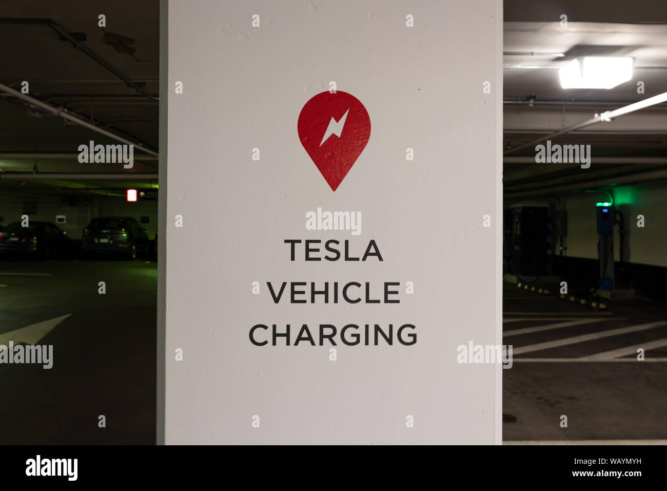 Tesla Supercharger logo and Tesla Vehicle Charging text on post in parking garage in-front of Tesla Supercharger Station. Stock Photo