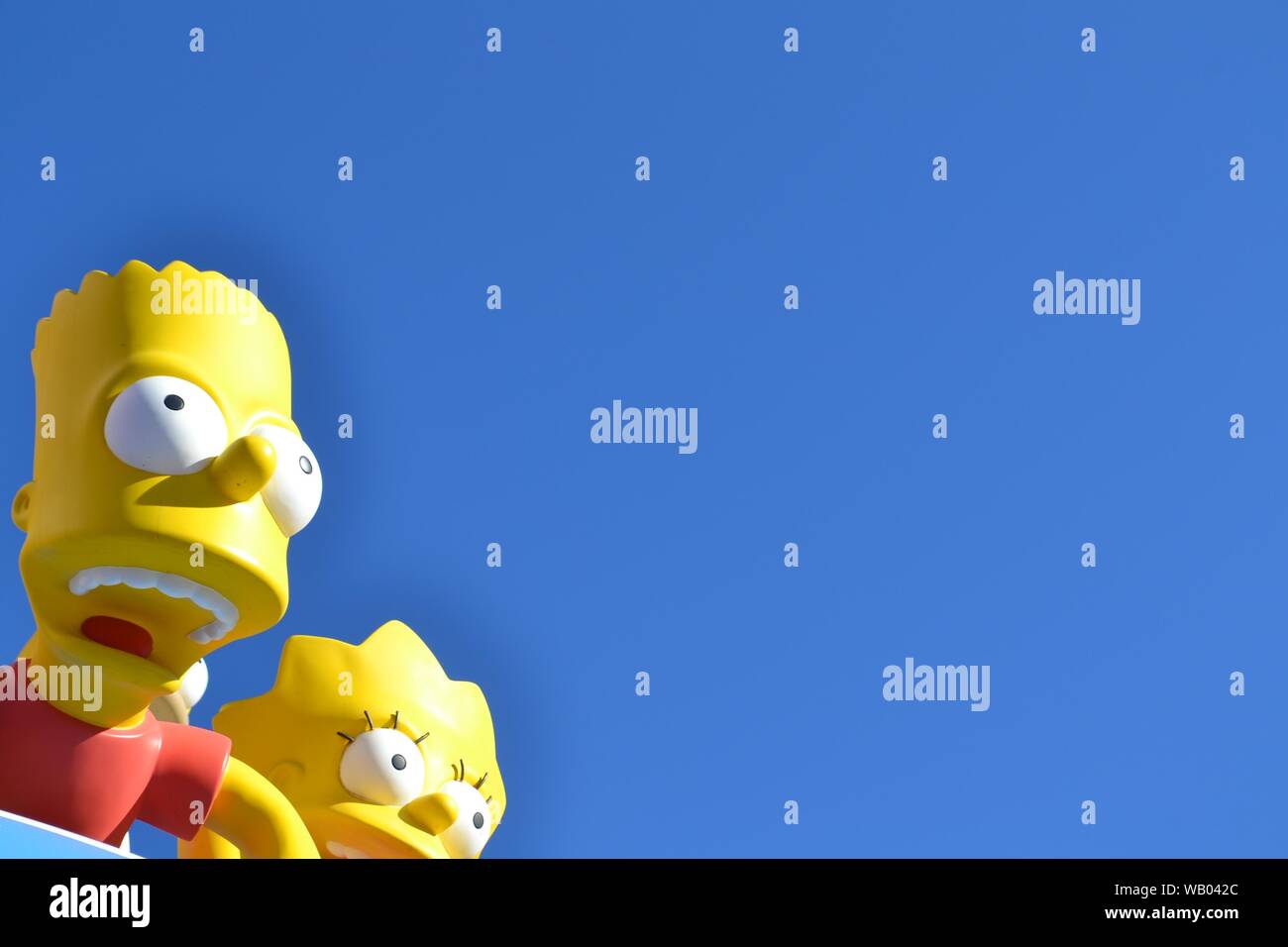 Slight closeup shot of Bart and Lisa Simpsons statues under a blue sky Stock Photo