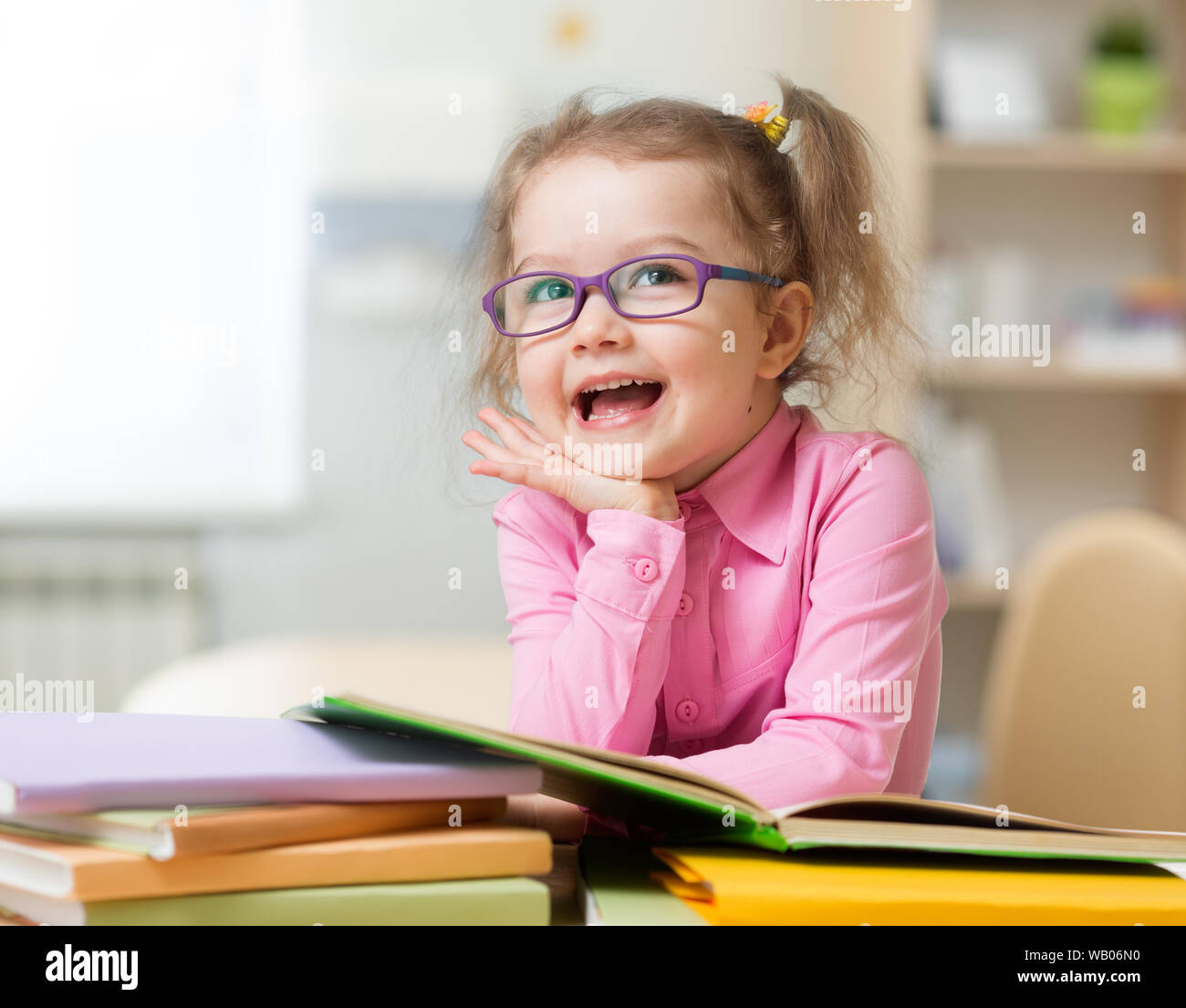 Smart kid girl in glasses reading books sitting at table at her room Stock Photo