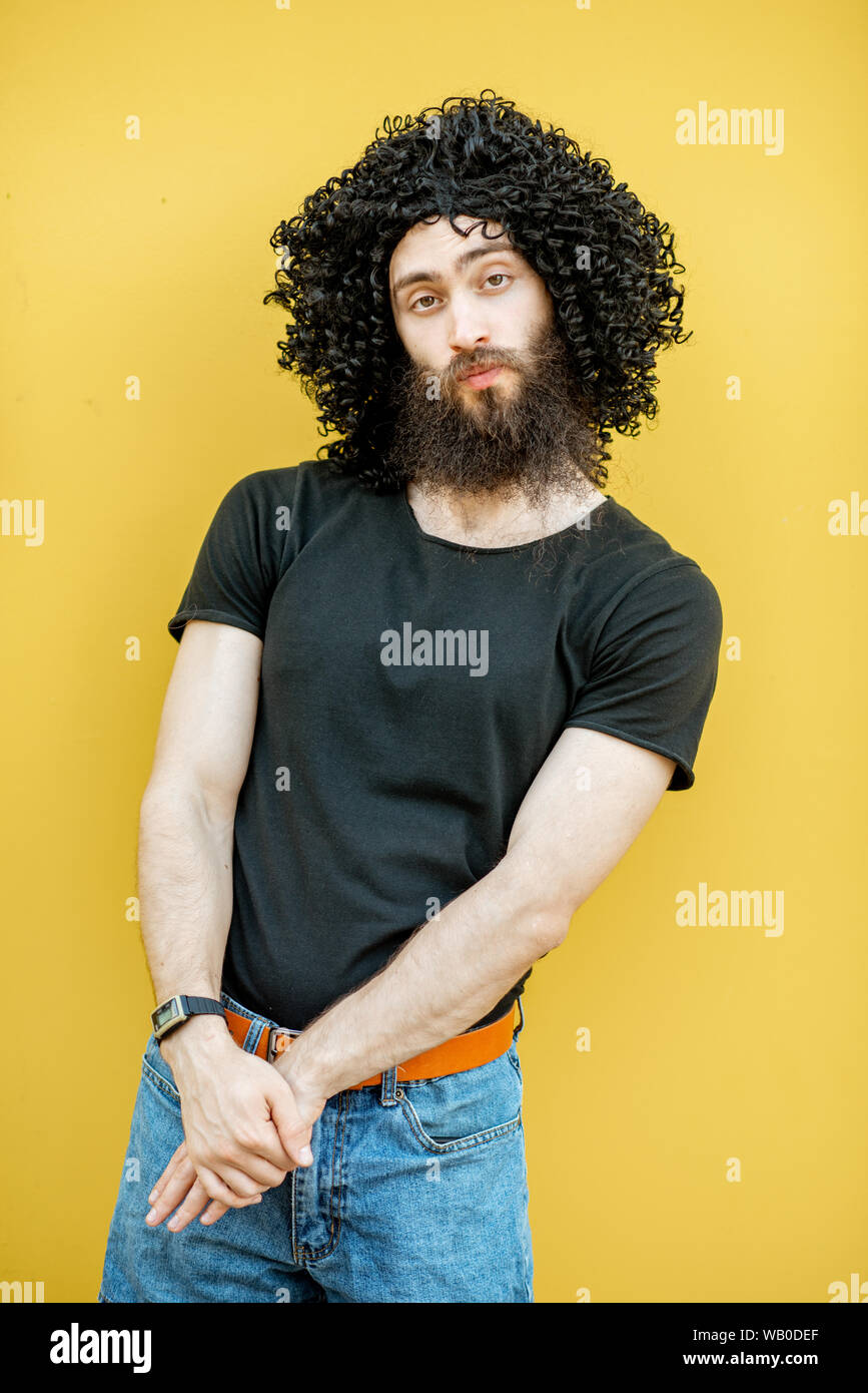 Portrait of a weird man with curley black hair standing on the yellow background Stock Photo