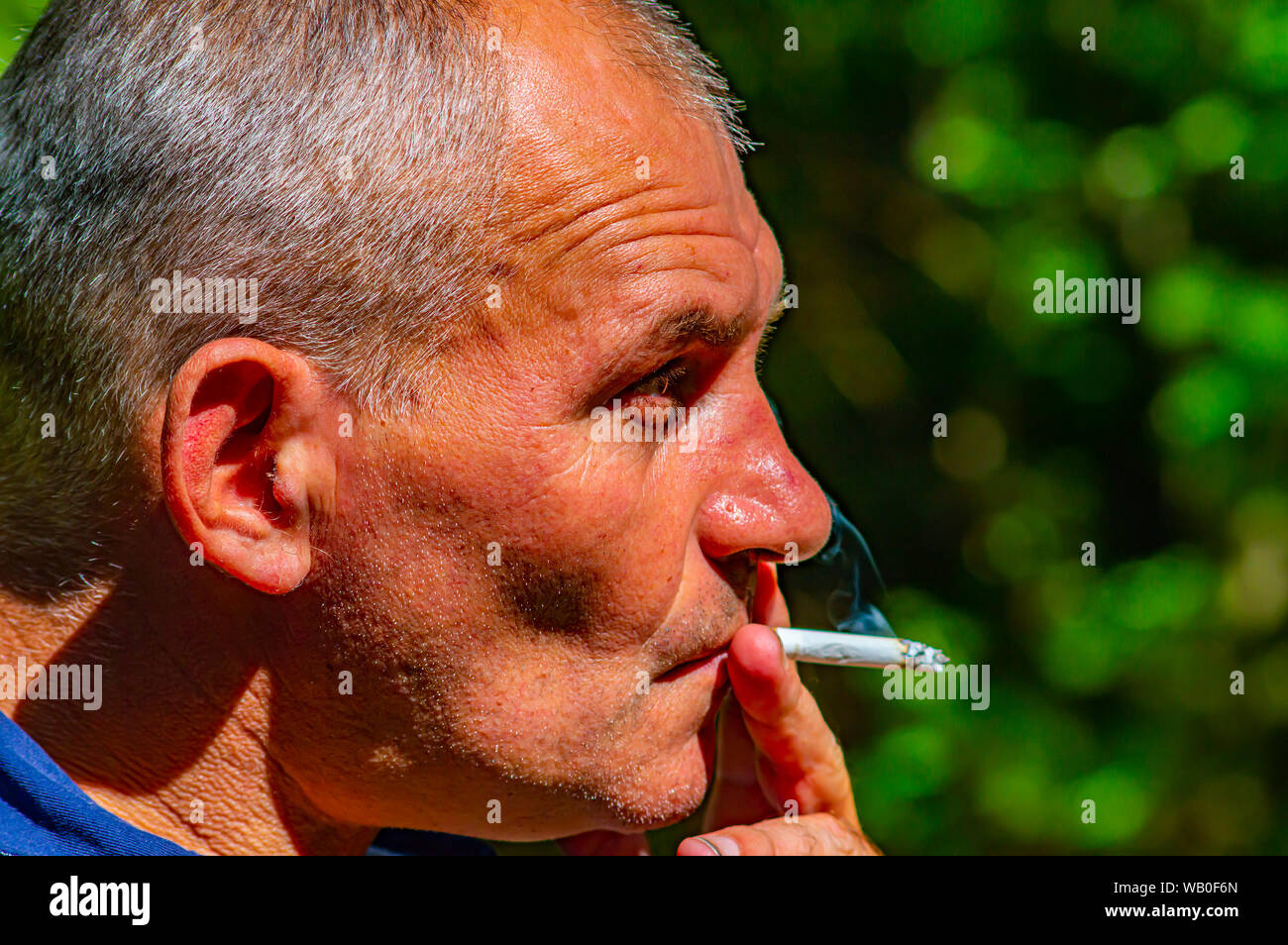 The gray-haired man smokes a cigarette. Outdoors. Mature age. Social problems. Health and medicine. Loneliness in old age. Stock Photo