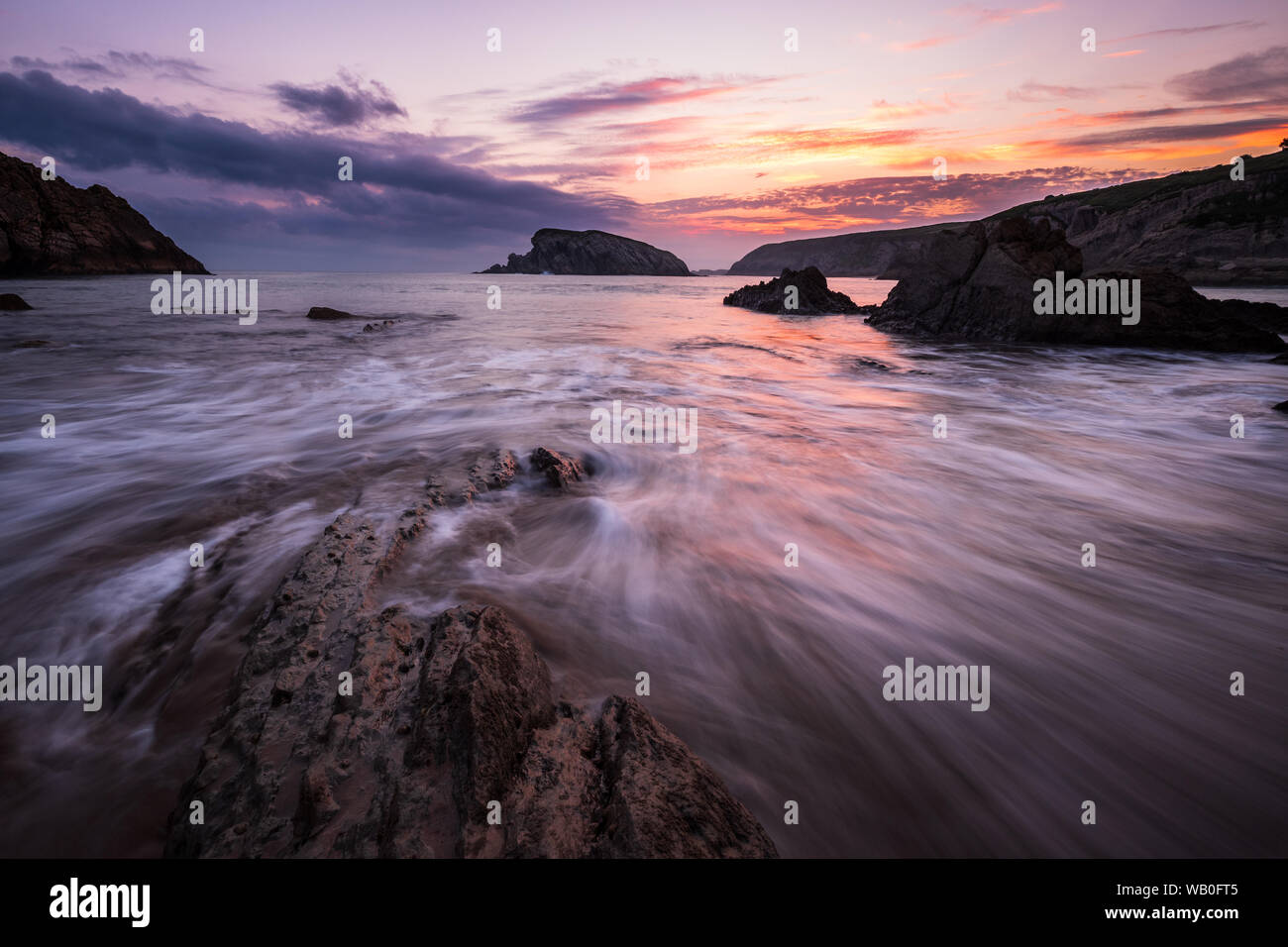 Colorful cloudy Sunrise at the beach of playa de la arnia with dynamic waves and bizarre rocks, Liencres, Northern Spain Stock Photo