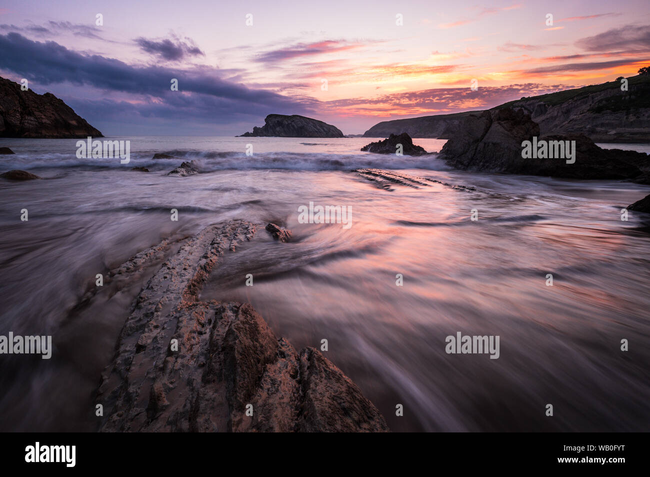 Colorful cloudy Sunrise at the beach of playa de la arnia with dynamic waves and bizarre rocks, Liencres, Northern Spain Stock Photo