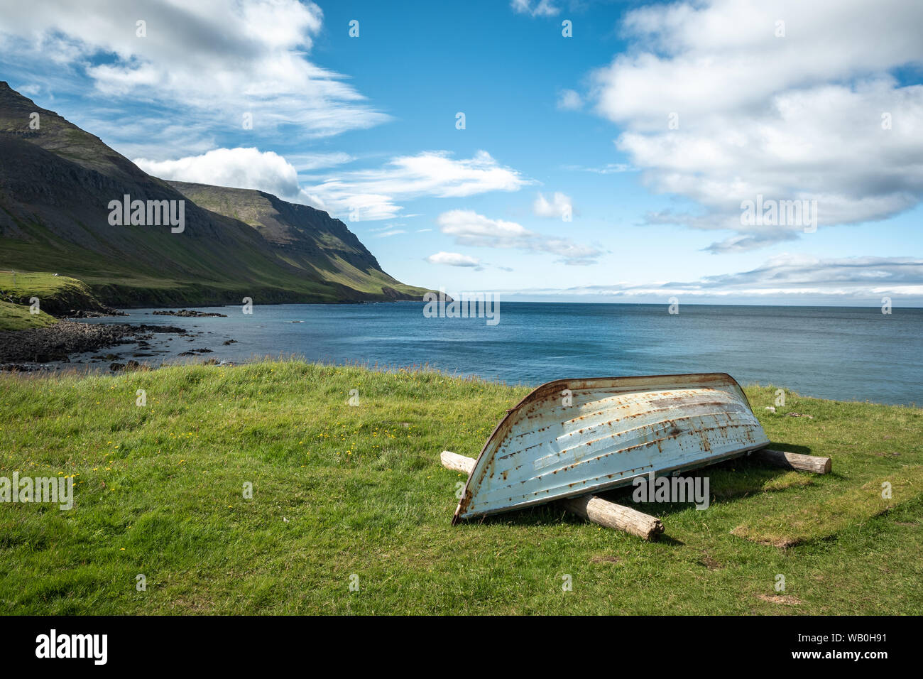 Old boat on meadow at the coast in the westfjords under blue sky with white clouds, Iceland Stock Photo