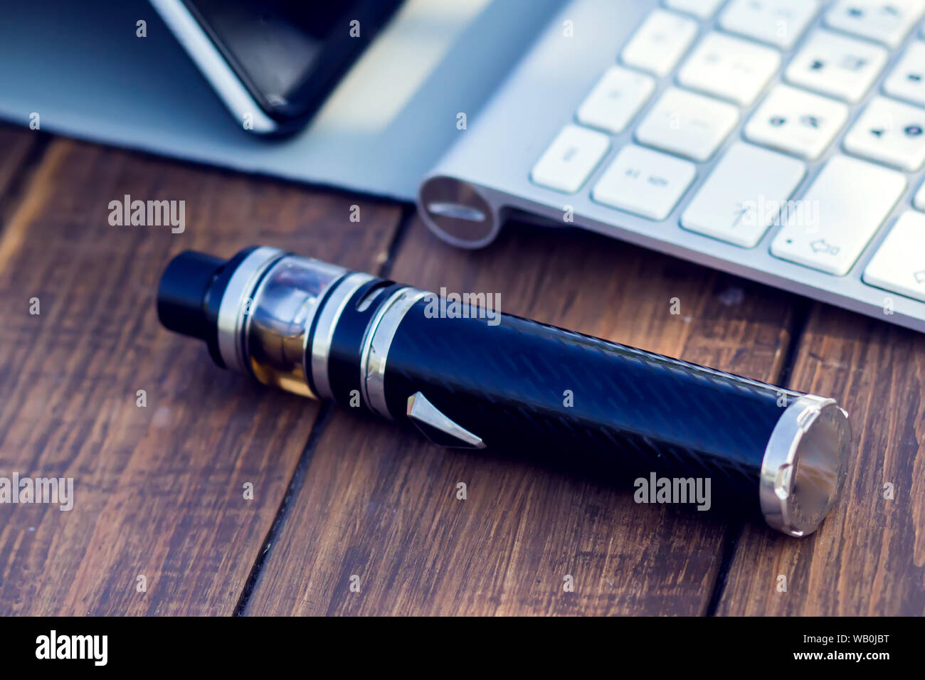 A vaporizer and laptop are on the wooden table. Smoke devise. Lifestyle concept Stock Photo
