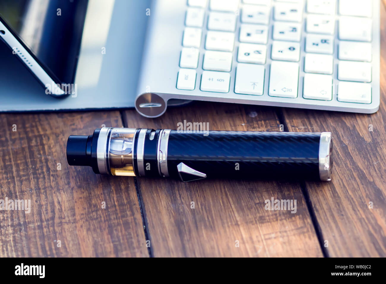 A vaporizer and laptop are on the wooden table. Smoke devise. Lifestyle concept Stock Photo