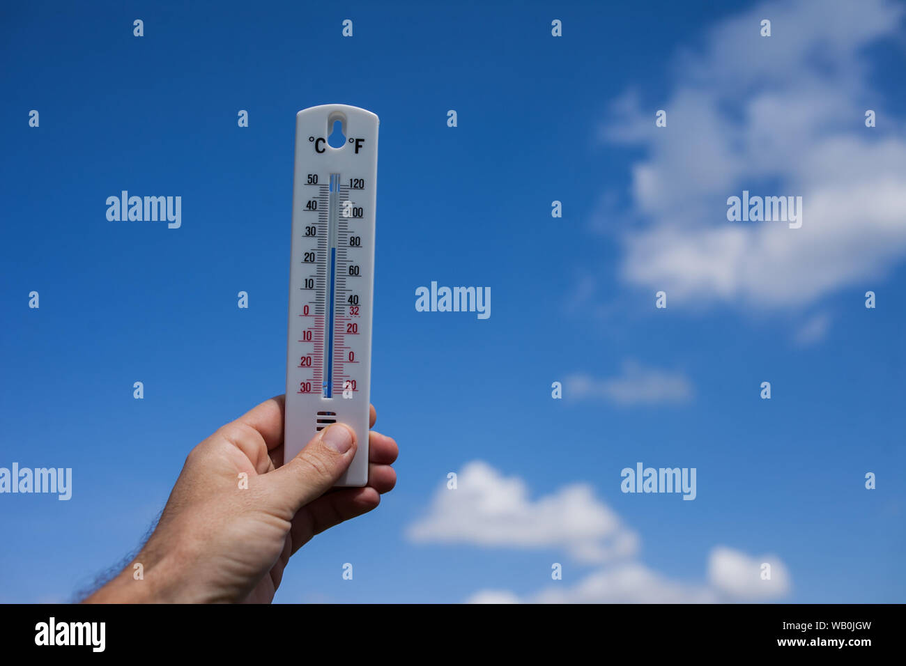 Man keep thermometer in hand at sky with clouds background. Weather concept Stock Photo