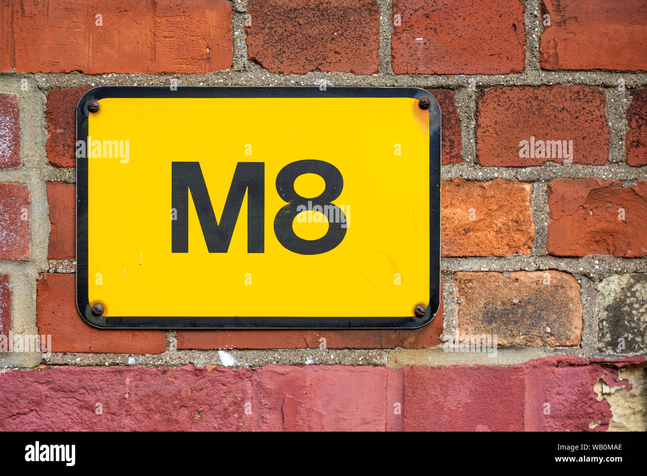 Letter M number 8 yellow sign on brick wall, used to spell Mate in text messages Stock Photo