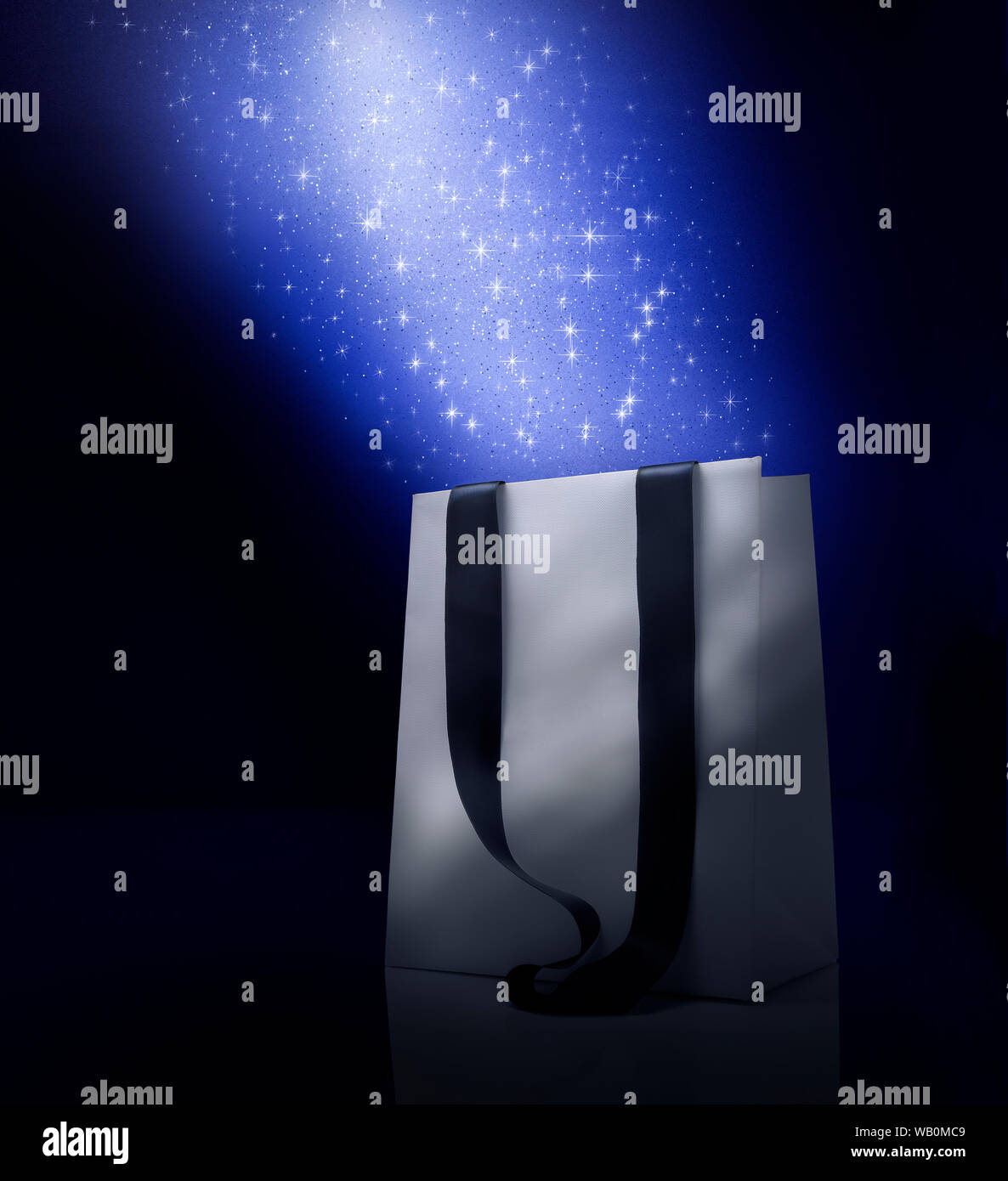 Fantasy Christmas shopping bag . Blue color stardust effect over white bag. Black background and copy space Stock Photo