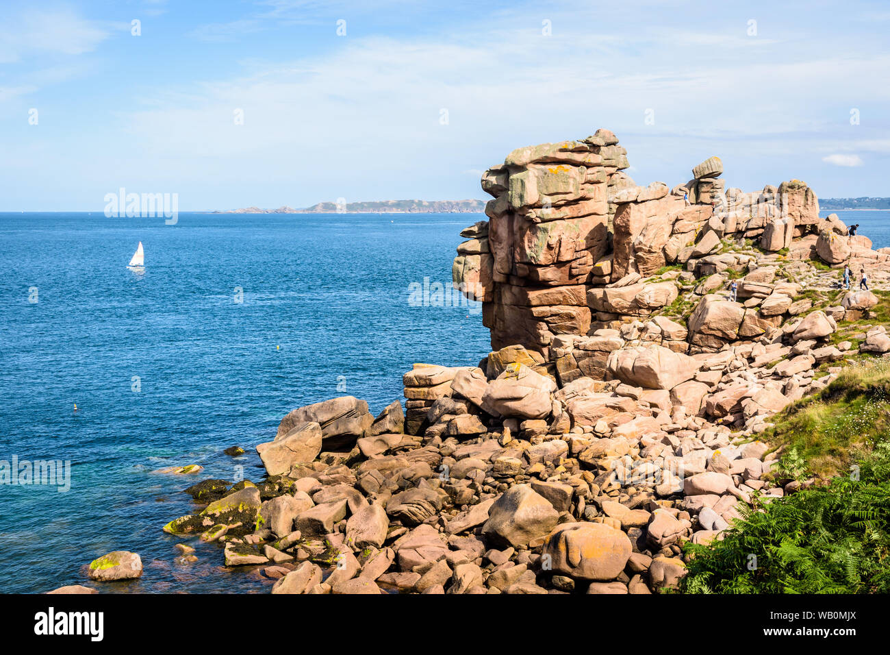 Granite blockfield on the Pink Granite Coast in northern Brittany, France, with a small catamaran sailing on the sea in the distance. Stock Photo