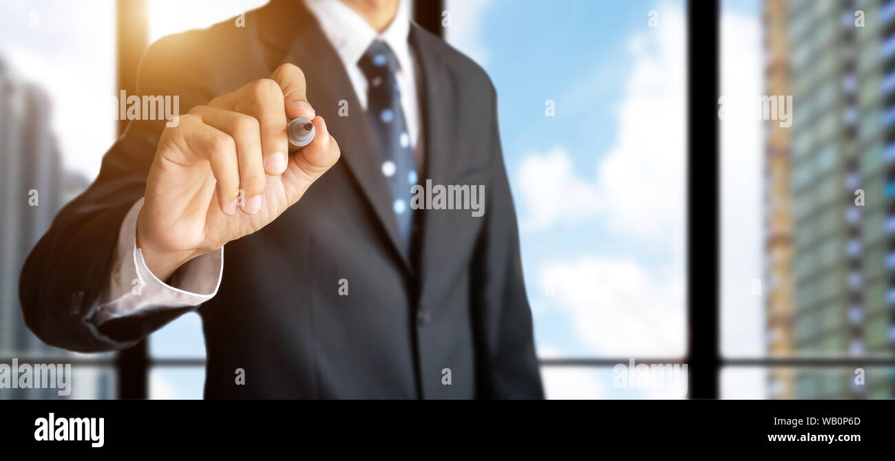 confident businessman hand holding black magic marker pen for write something , office work space with building for city background Stock Photo