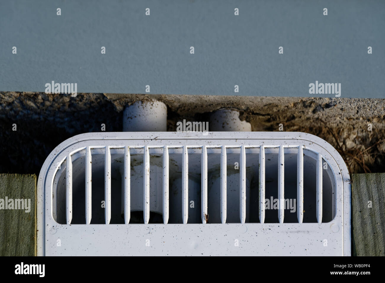 A plastic drain cover at the side of a house, the pipes can be seen exiting the building Stock Photo