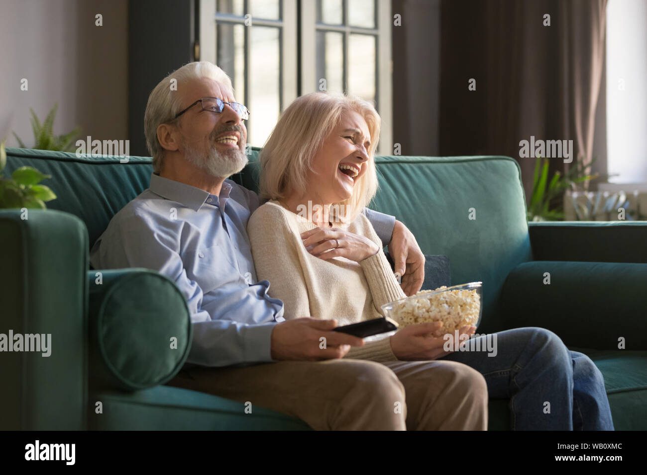 Cheerful old couple holding remote control laughing watching funny tv Stock Photo