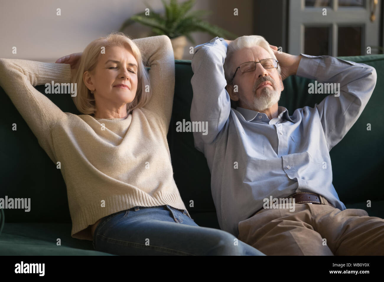Calm old couple relaxing on sofa enjoy daytime nap together Stock Photo