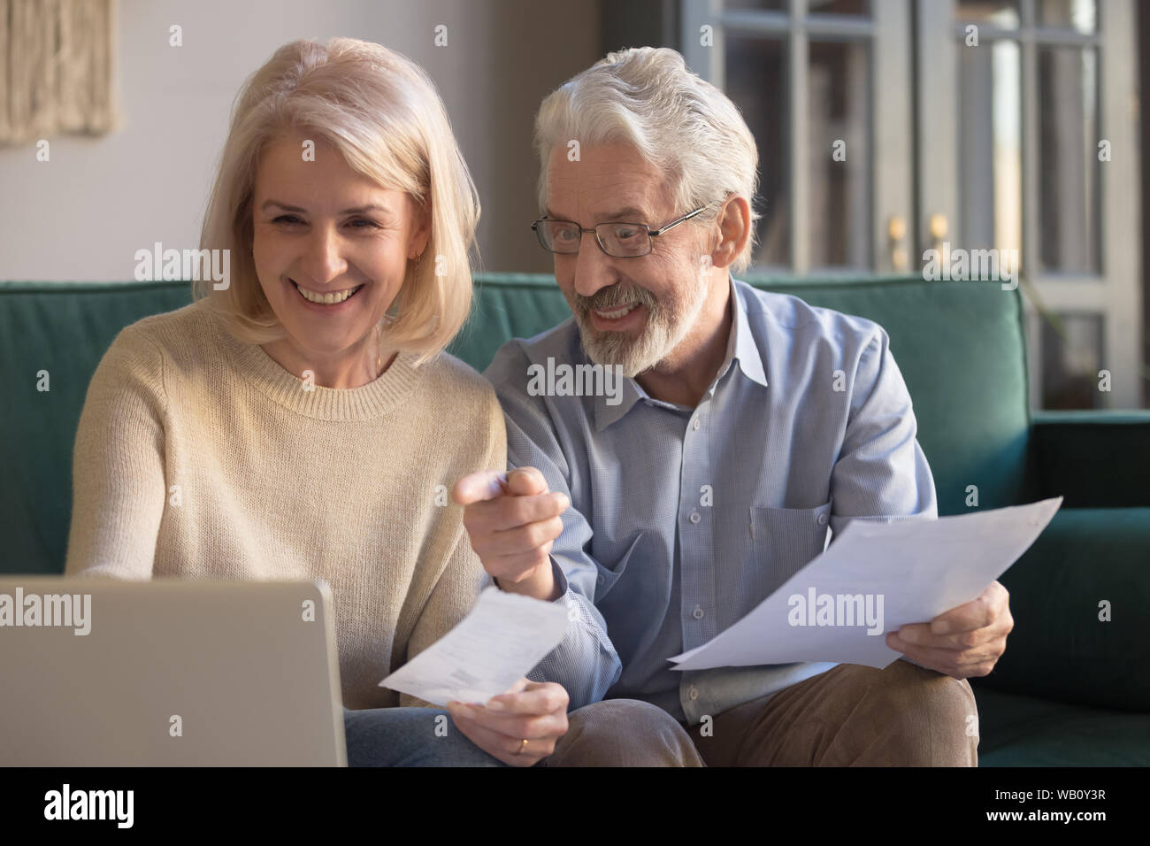 Happy old couple paying domestic bills online using computer app Stock Photo