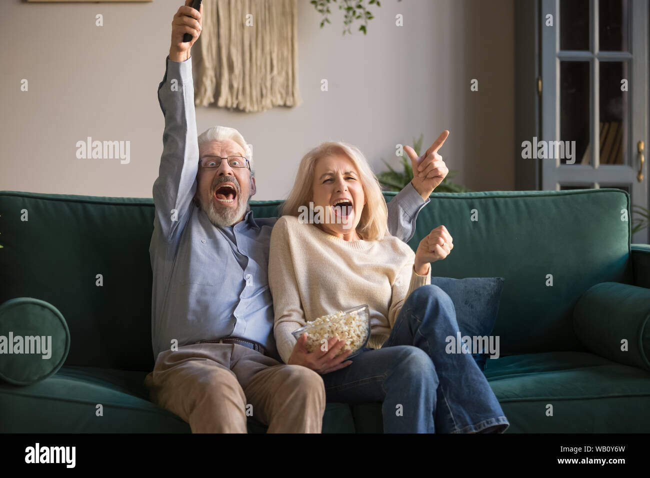 Excited old couple holding remote control watching tv celebrate victory Stock Photo