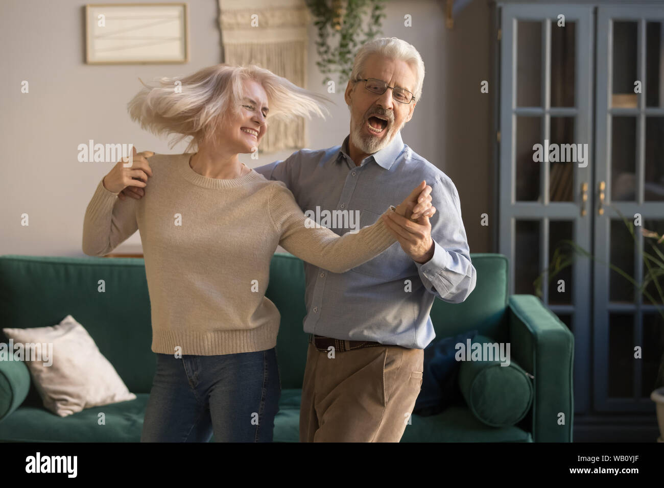 Carefree happy active old couple dancing laughing in living room Stock Photo