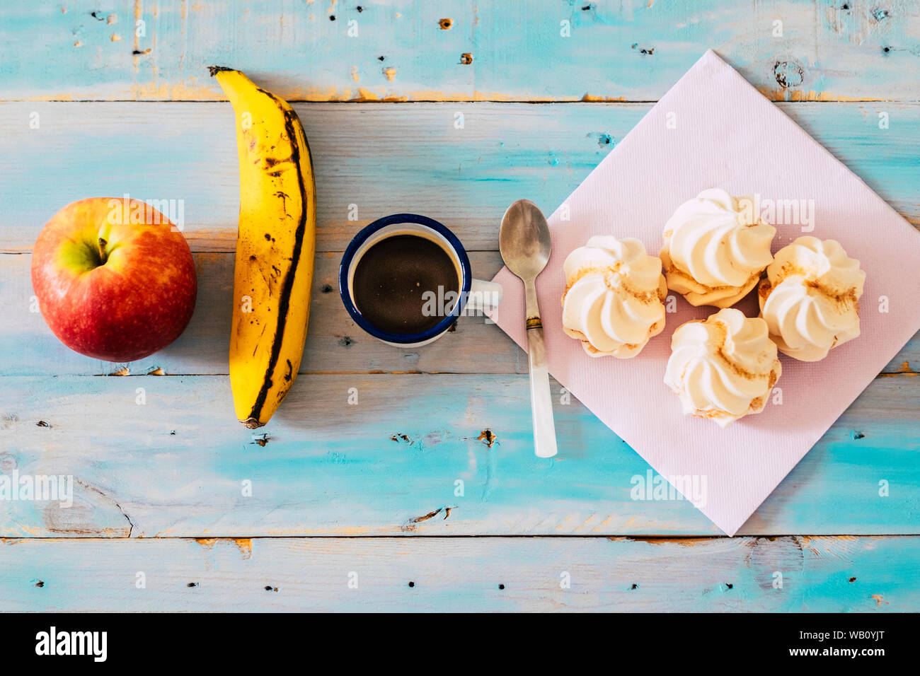 coloured background with fresh food - closeup of some food in a blue table background - table of wood with an apple, banana, coffe and macarones on it Stock Photo