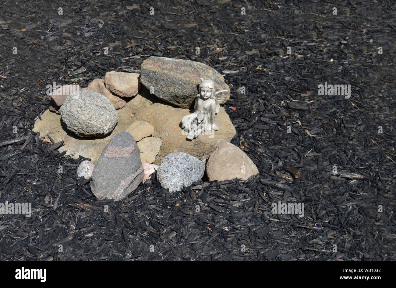 Lawn and garden ornament of an angel on decorative rocks.  The little angel guards the garden from bad weeds. Landscaping with mulch. Stock Photo