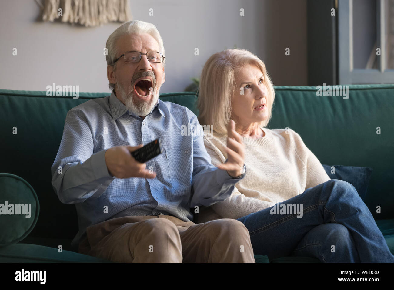 Bored middle-aged wife annoyed with senior husband watching sport tv Stock Photo