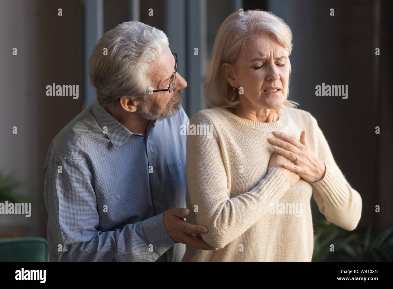 Worried elder husband helping wife touching chest having heart attack Stock Photo
