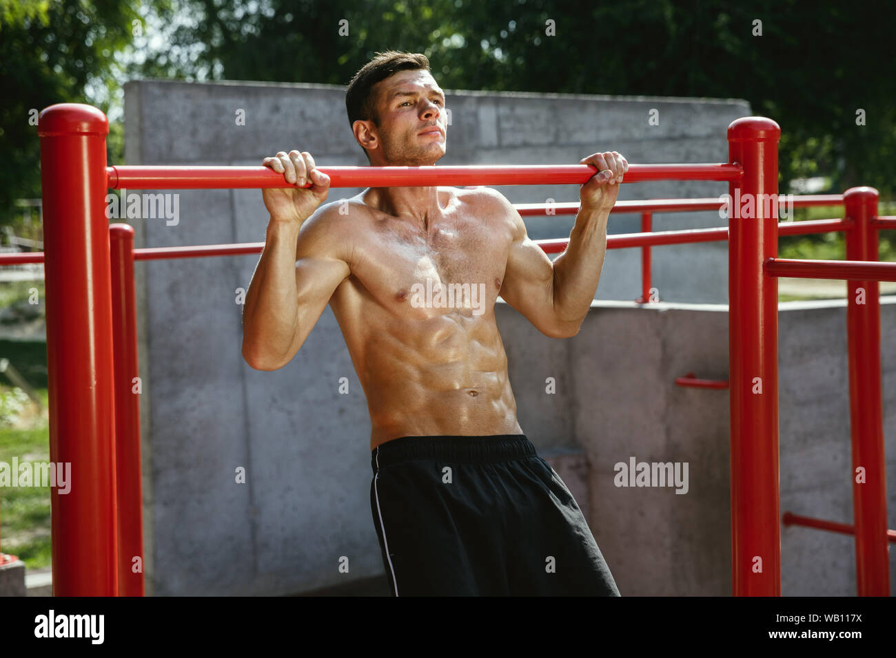 Young muscular shirtless caucasian man doing pull-ups on horizontal bar ...