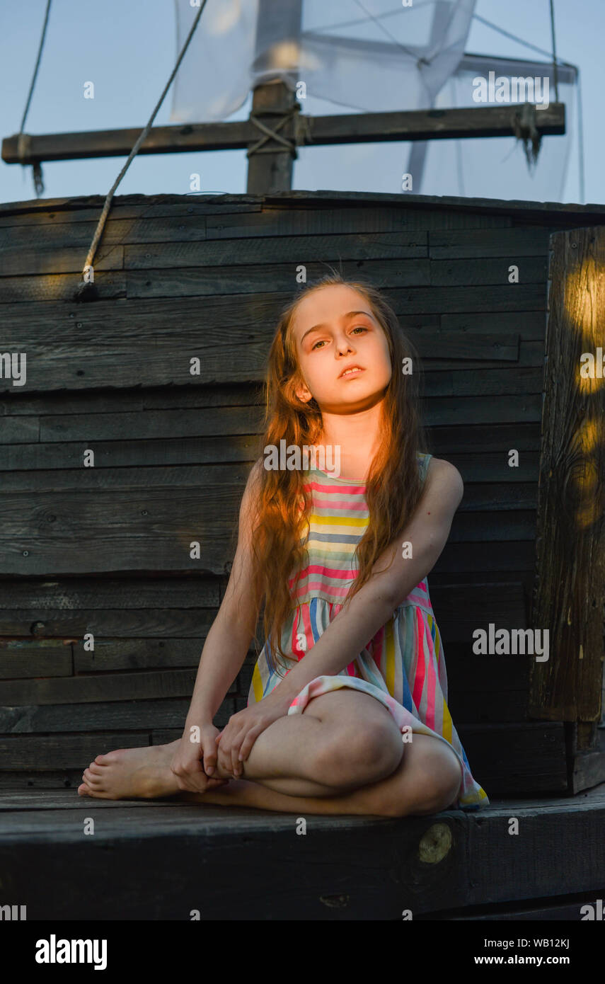 Pensive Little Child With Long Hair Resting On Wooden Deck