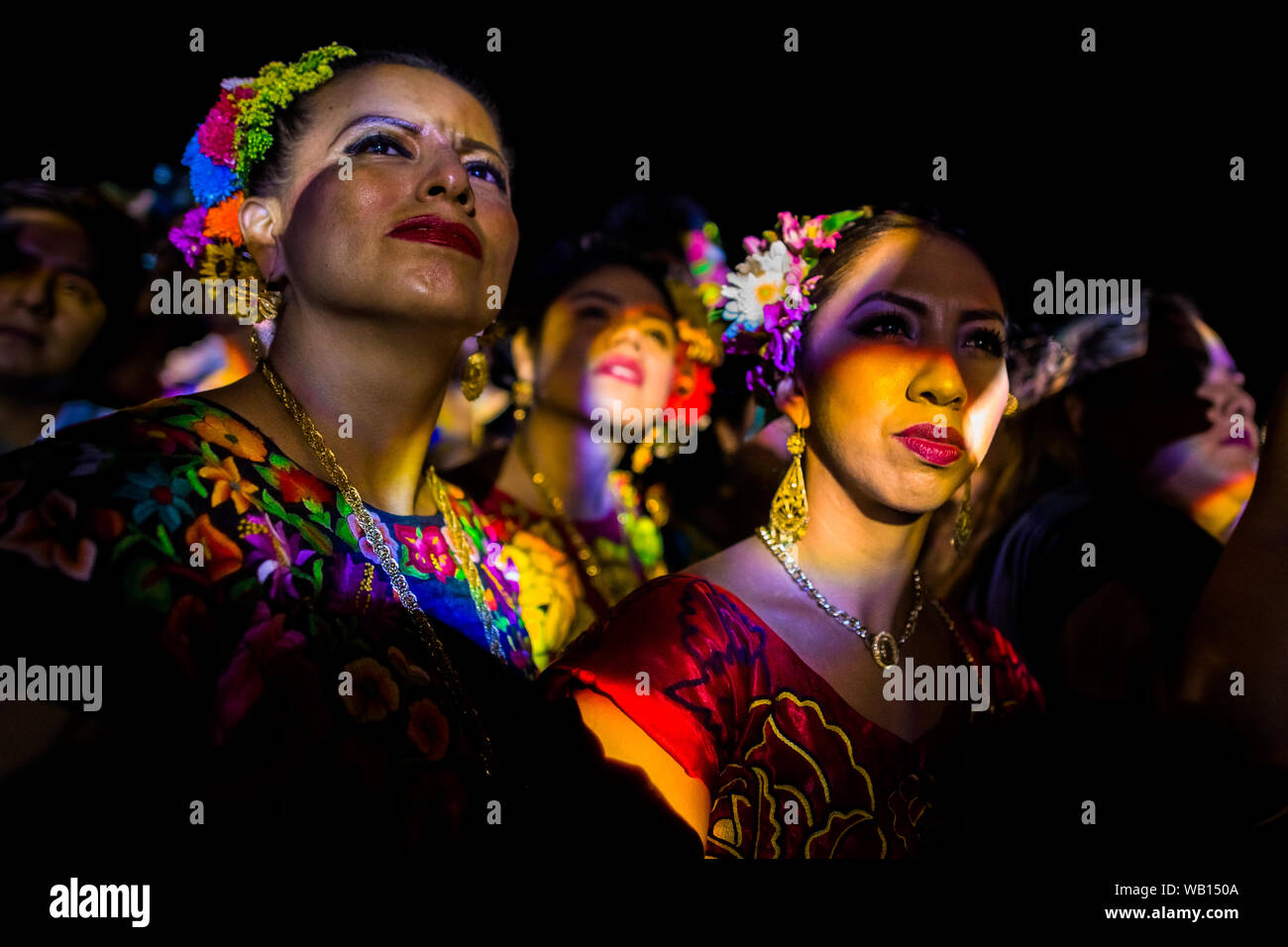 Mexican women of Zapotec origin, wearing traditional Tehuana dress, watch the party stage during the festival in Juchitán de Zaragoza, Mexico. Stock Photo